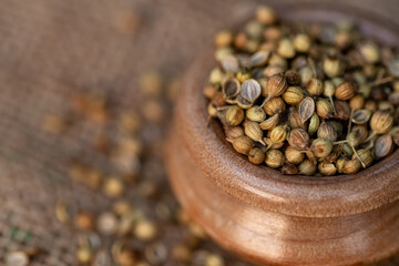 Closeup of dried coriander seeds in a wooden bowl on a textured surface, macro photography