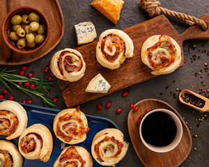 savory bakery rolls with sausage slices, blue cheese, hard cheese, black pepper, olives and coffee on rustic wooden serving boards, festive homemade snack, cozy kitchen appetizer in daylight