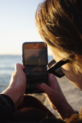 Person taking a picture of the ocean with a smartphone at sunset