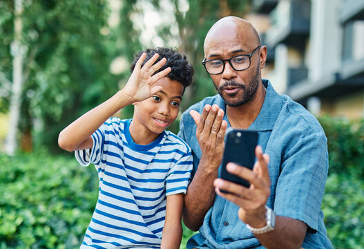 Portrait of father and son having fun using a mobile phone and taking a selfie photo with camera outdoors in park or nature,, family life, parenting, love and bonding concepts
