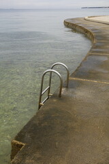 Coastal concrete pier with a metal ladder leading into the calm, clear water