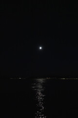 Full moon over the ocean at night with city lights on the horizon