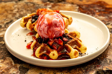 waffles, ice cream and strawberry slices served on a plate on a wooden table
