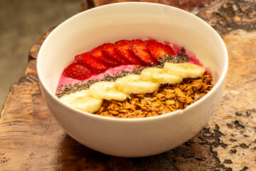 a sprinkling of nuts, a few slices of banana and a few pieces of strawberries served in one bowl on a wooden table