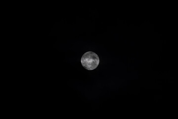 Obraz premium A close-up of the bright full Moon against the deep black night sky, with some clouds. The lunar disk is sharp and detailed, with the texture of the craters and lunar maria clearly visible.