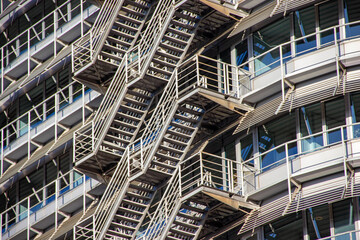 Modern architectural design featuring metallic fire escape stairs attached to a contemporary building with large glass windows showcasing urban living and safety features
