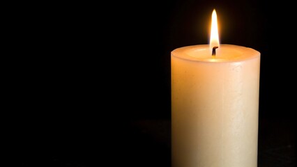 A lit white candle with a flame against a black background