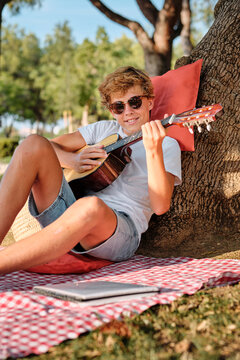 Teenager playing guitar in the park under a tree