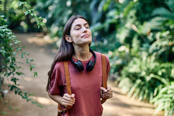 Young woman with backpack enjoying a sunny day visiting a botanical garden, surrounded by trees and...