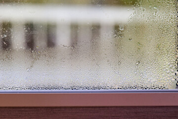 Macro image of water condensation and dripping streaks on a window pane. Household energy loss, poor insulation, and environmental impact.