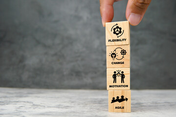 Wooden cubes stacked vertically with icons representing flexibility, change, motivation, and agile...