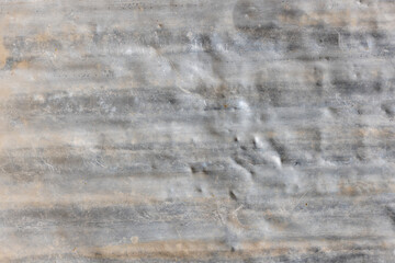 Close-up of a weathered gray corrugated aluminum sheet shows signs of age with visible dents and scratches. The grunge texture highlights rustic charm in an outdoor setting.