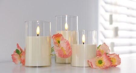 Decorative LED candles and beautiful flowers on white table indoors, closeup