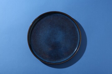 Stylish ceramic plate on blue background, top view
