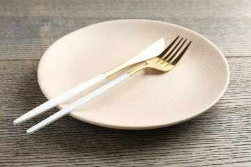 Clean ceramic plate and cutlery on wooden table, closeup