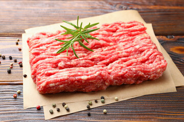 Raw minced meat with peppercorns and rosemary on wooden table, closeup