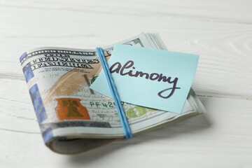 Note with word Alimony and money on white wooden table, closeup