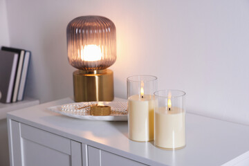 Decorative LED candles, lamp and jewellery on white cabinet indoors