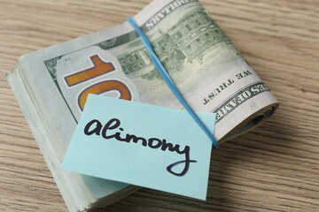 Note with word Alimony and money on wooden table, closeup