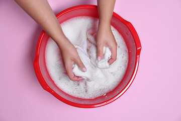Woman washing clothes in plastic basin on pink background, top view