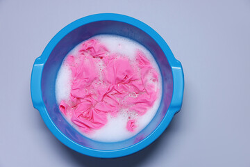 Plastic basin with clothes, water and foam on light grey background, top view