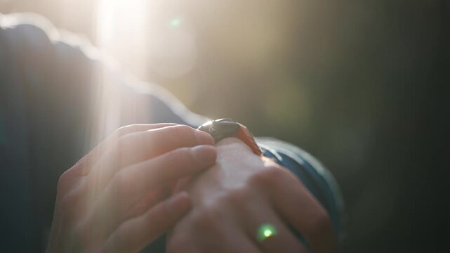Closeup of a male athlete's hands using a smartwatch to track performance and heart rate during training in a park, with beautiful sunlight creating a lens flare in the background