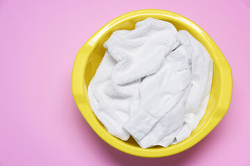 Plastic basin with clothes on pink background, top view