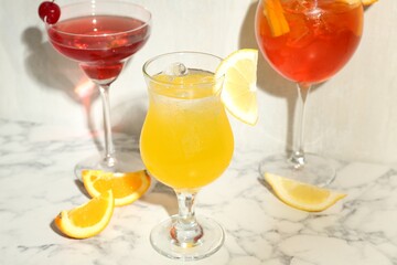 Glasses of tasty cocktails with garnish on white marble table, closeup
