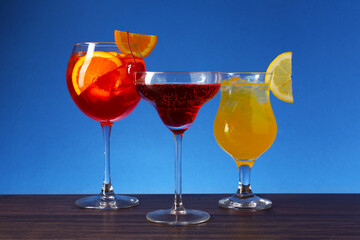 Glasses of tasty cocktails with garnish on wooden table against blue background