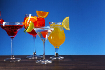 Glasses of tasty cocktails with garnish on wooden table against blue background, space for text