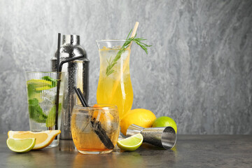 Glasses of tasty cocktails, ingredients, shaker and jigger on grey table, space for text