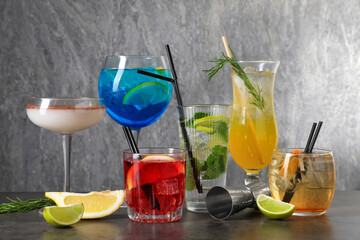 Glasses of tasty cocktails, ingredients and jigger on grey table