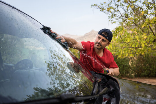 Man washing SUV windshield by hand outdoors