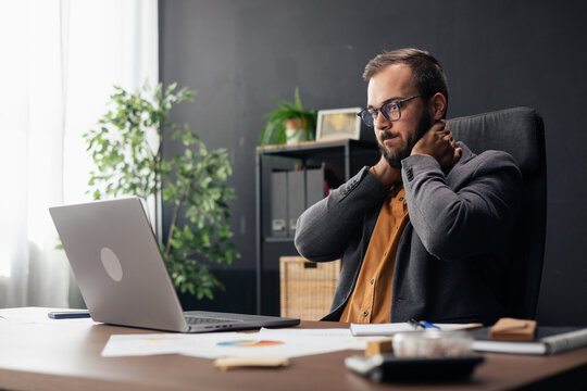 Stressed businessman feeling neck pain working at office desk