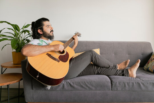 Man relaxing and playing guitar on couch at home