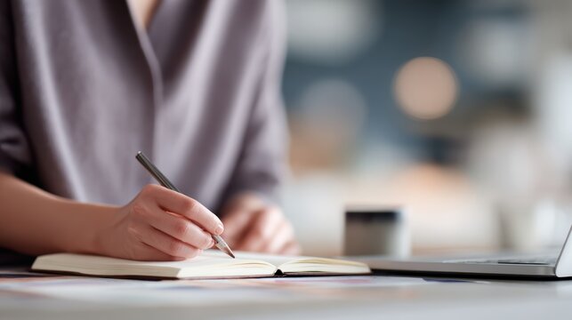 A creative designer sketching fresh ideas in a notebook at a lively co-working space, with a laptop open next to them. - Powered by Adobe