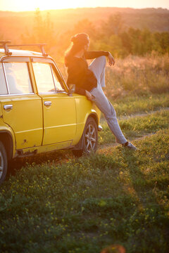 A guy near an old yellow car, looking at the sunset, evening time, sun rays, nature.