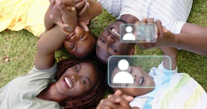 Family lying on grass raising interlocked hands, initiating floating tech icons tracking hand pairs