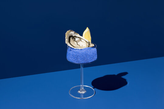 Oyster with lemon in cocktail glass on blue background
