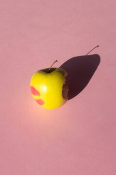 Apple with a bite and lipstick stain on pink background