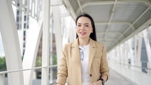 Determined businesswoman on pedestrian bridge holding tablet and walking confidently. Represents focus and strength.