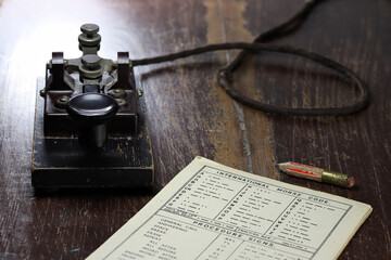 morse key with morse code chart on desk