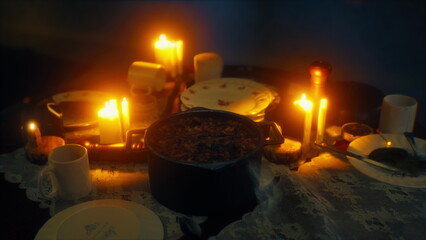 A warm and inviting dinner scene features a pot of stew surrounded by flickering candles. The table is set with plates and cups, creating a cozy atmosphere for a delightful meal.