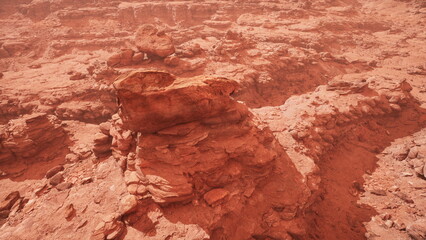 A stunning view reveals an expansive red desert filled with unique rock formations. The warm sunlight casts shadows, enhancing the textures and colors of the rugged terrain.