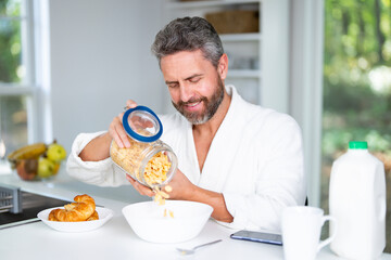 Man eats breakfast in the kitchen on a morning. Middle aged man enjoys fresh food at the kitchen table. A man eats cereal and fruit in the kitchen. Guy enjoys eggs and vegetables at the cozy kitchen.