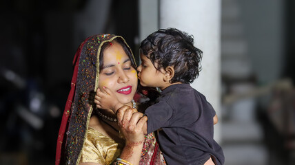 Fototapeta premium Indian mother wearing traditional saree lovingly holding her little son who kisses her cheek, showing affection, warmth, and beautiful motherhood moment
