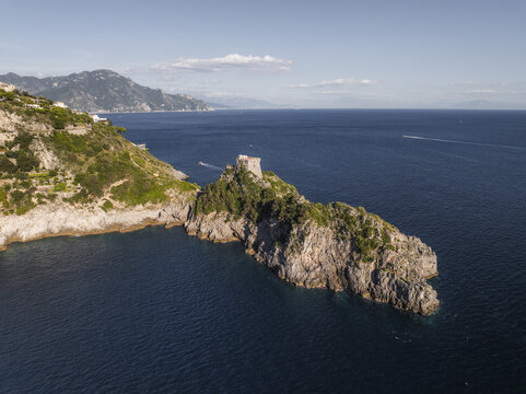 Aerial view of the craggy coastline meeting the deep blue sea, with a historic tower perched atop a rocky outcrop, a testament to time's passage, Conca dei Marini, Amalfi Coast, Campania, Italy.