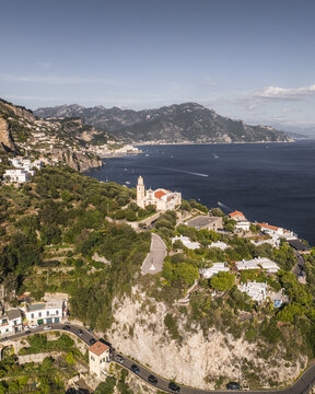 Aerial view of a church standing tall amidst the green landscape and winding roads overlooking the deep blue sea, Conca dei Marini, Amalfi Coast, Italy.