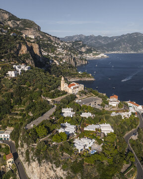 Aerial view of the Church of San Pancrazio standing majestically on the rugged coastline, with winding roads snaking through the verdant landscape, Conca dei Marini, Amalfi Coast, Campania, Italy.