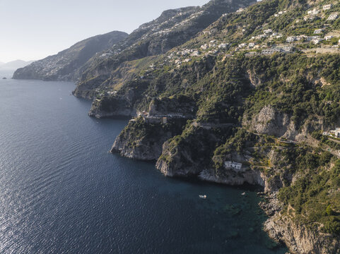 Aerial view of the Amalfi Coast's rugged cliffs plunging into the deep blue sea, dotted with white buildings clinging to the verdant slopes, Conca dei Marini, Amalfi Coast, Campania, Italy.